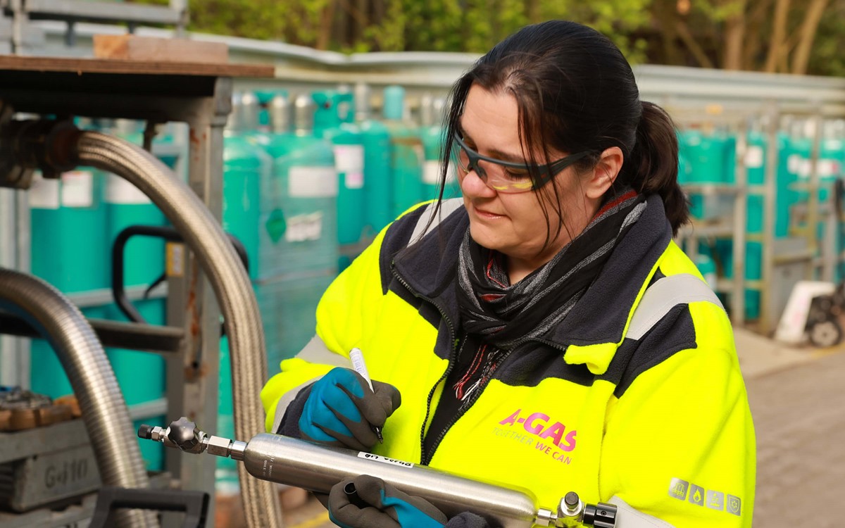 A woman in a yellow high-vis jacket writing on a metal piece of equipment
