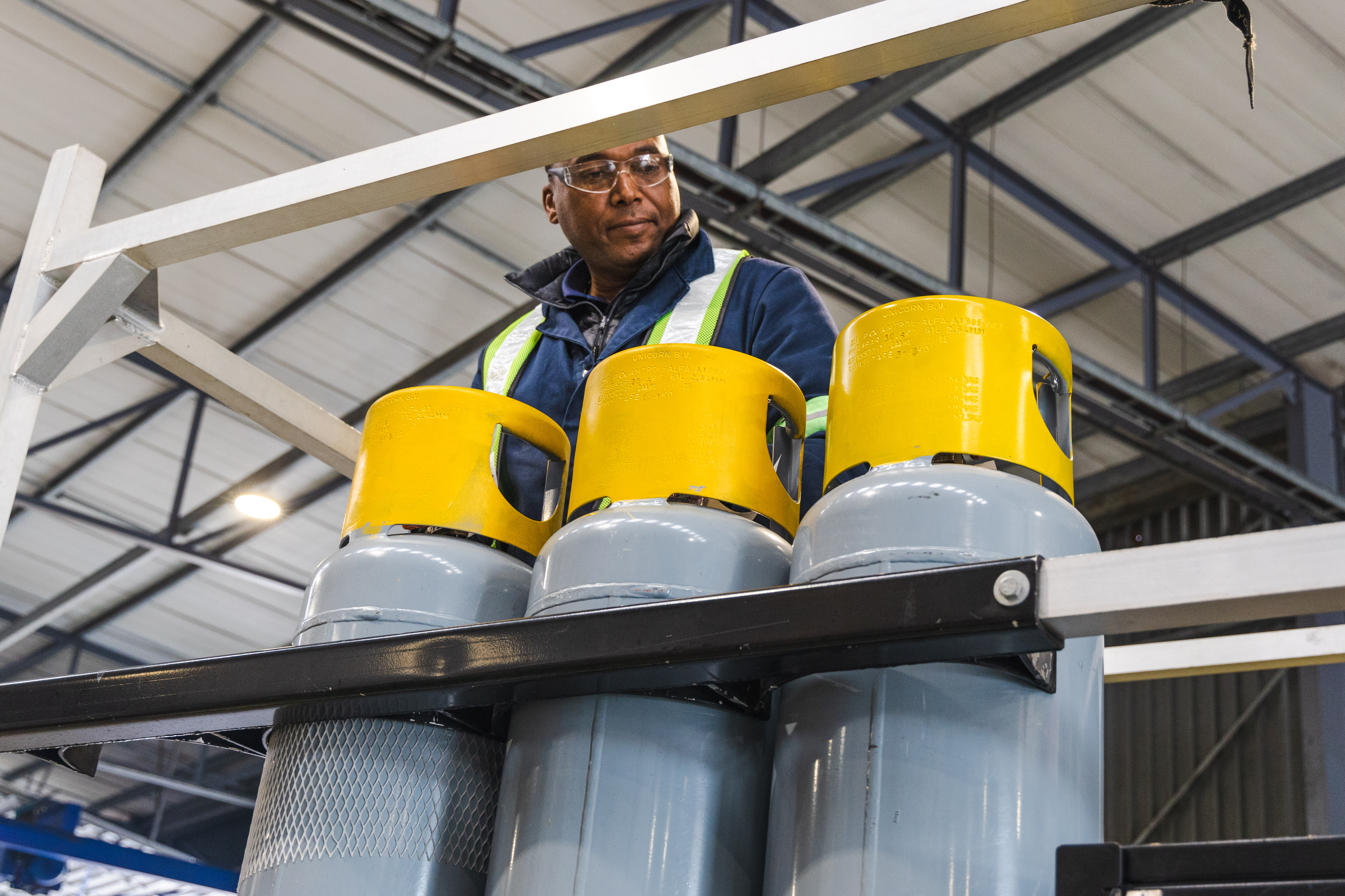 An A-Gas technician works on a row of grey cylinders with yellow tops in a warehouse 