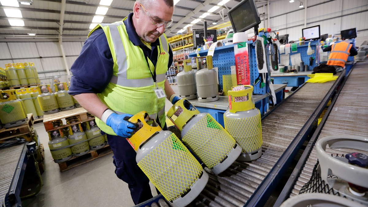 A man working in a warehouse, he is wearing a hi vis jacket and moving gas cylinders