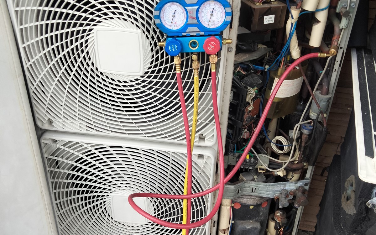 A close up of a white air conditioning unit with recovery hosing attached to it