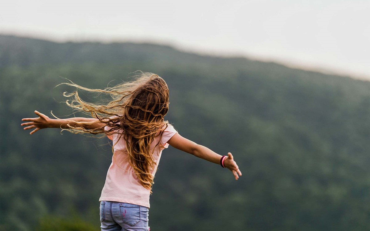 young girl outdoors with arms wide open