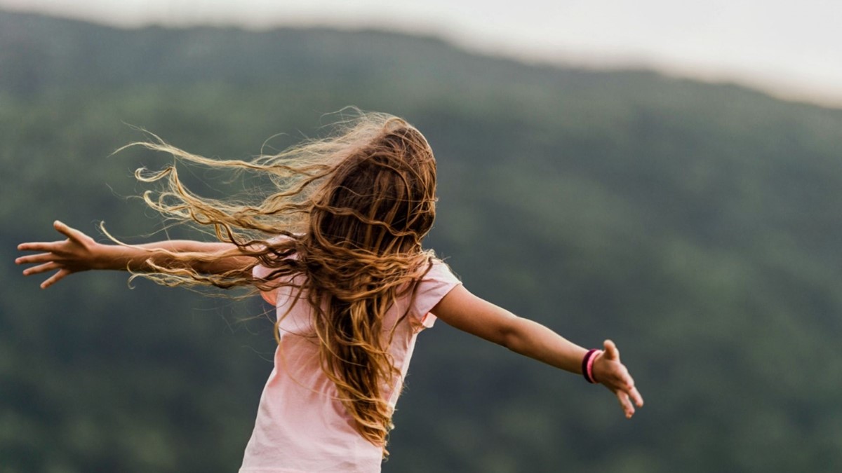 young girl with back to camera with arms wide open embracing nature