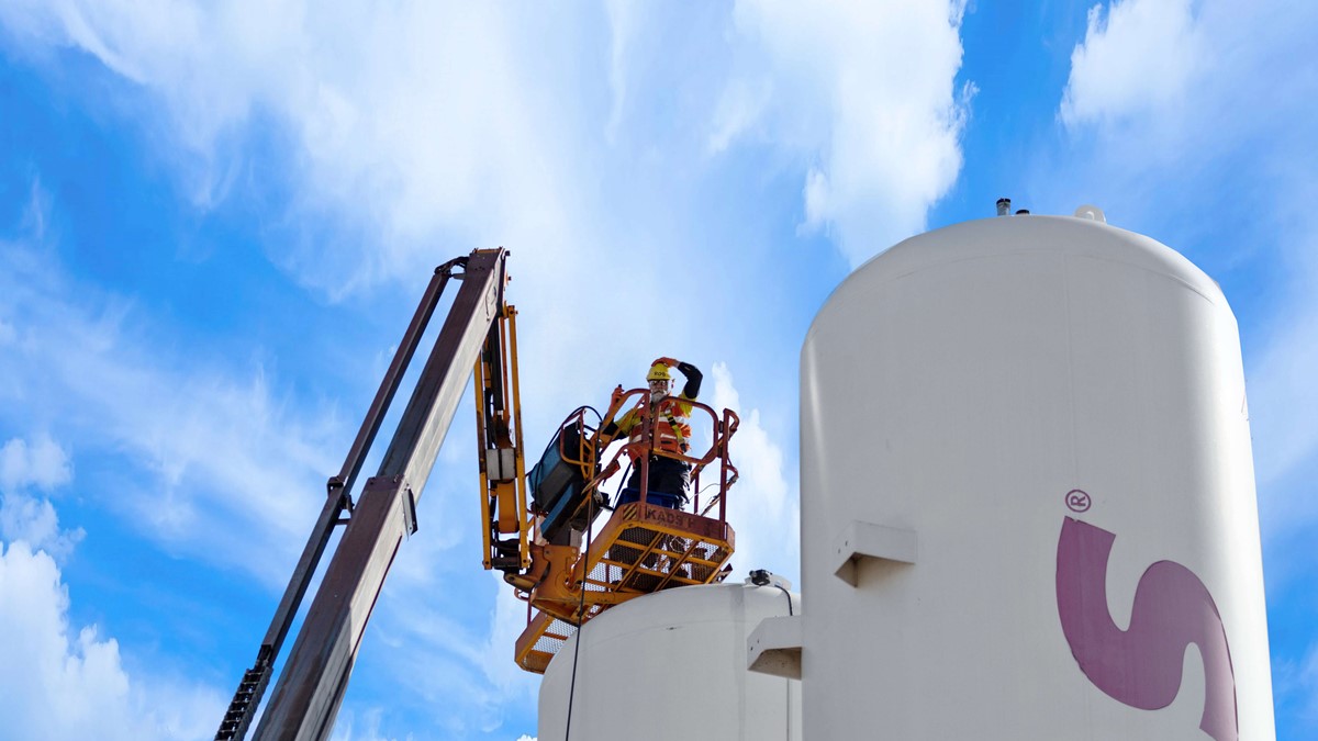 Three white separation towers beneath an operator in high-vis clothing on a crane