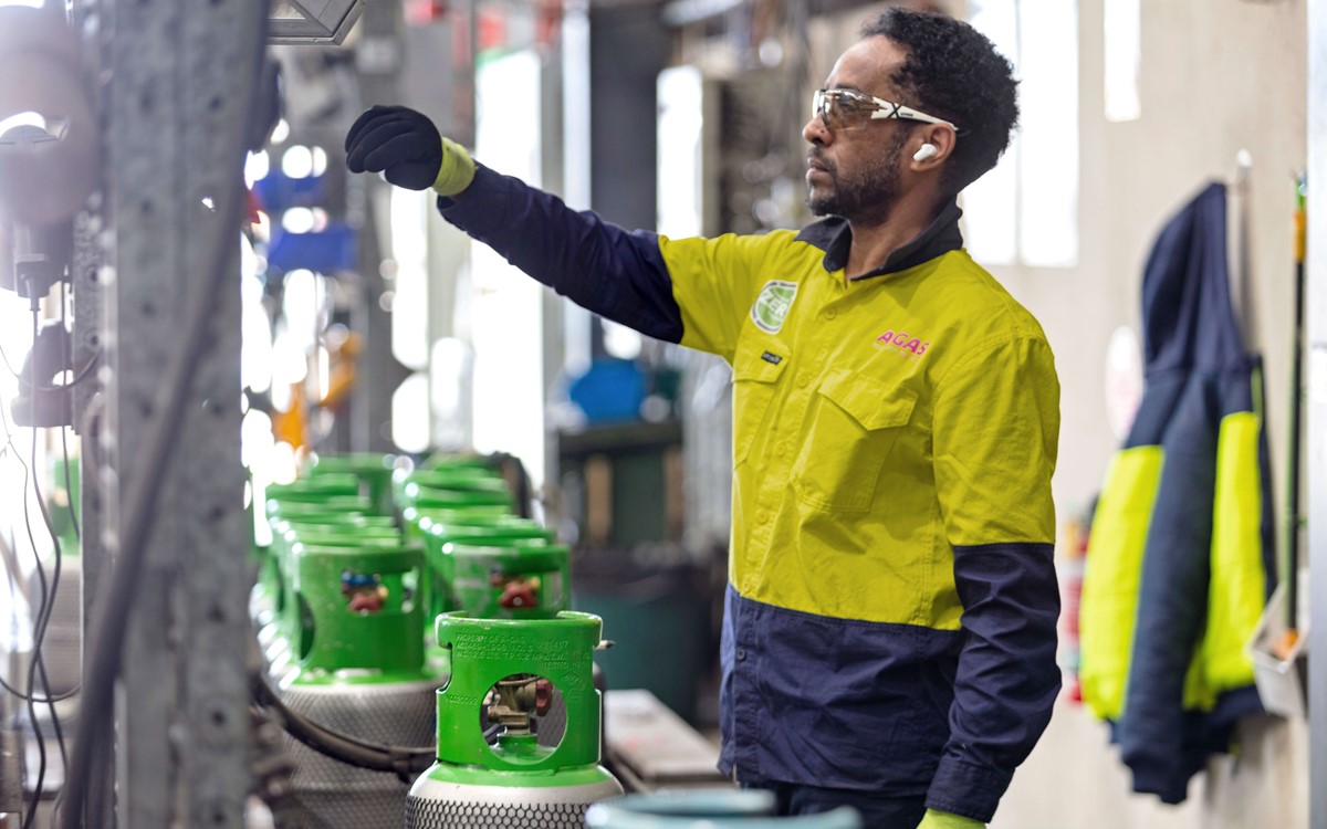 Technician in a yellow and blue high-vis jacket filling a green-topped gas cylinder