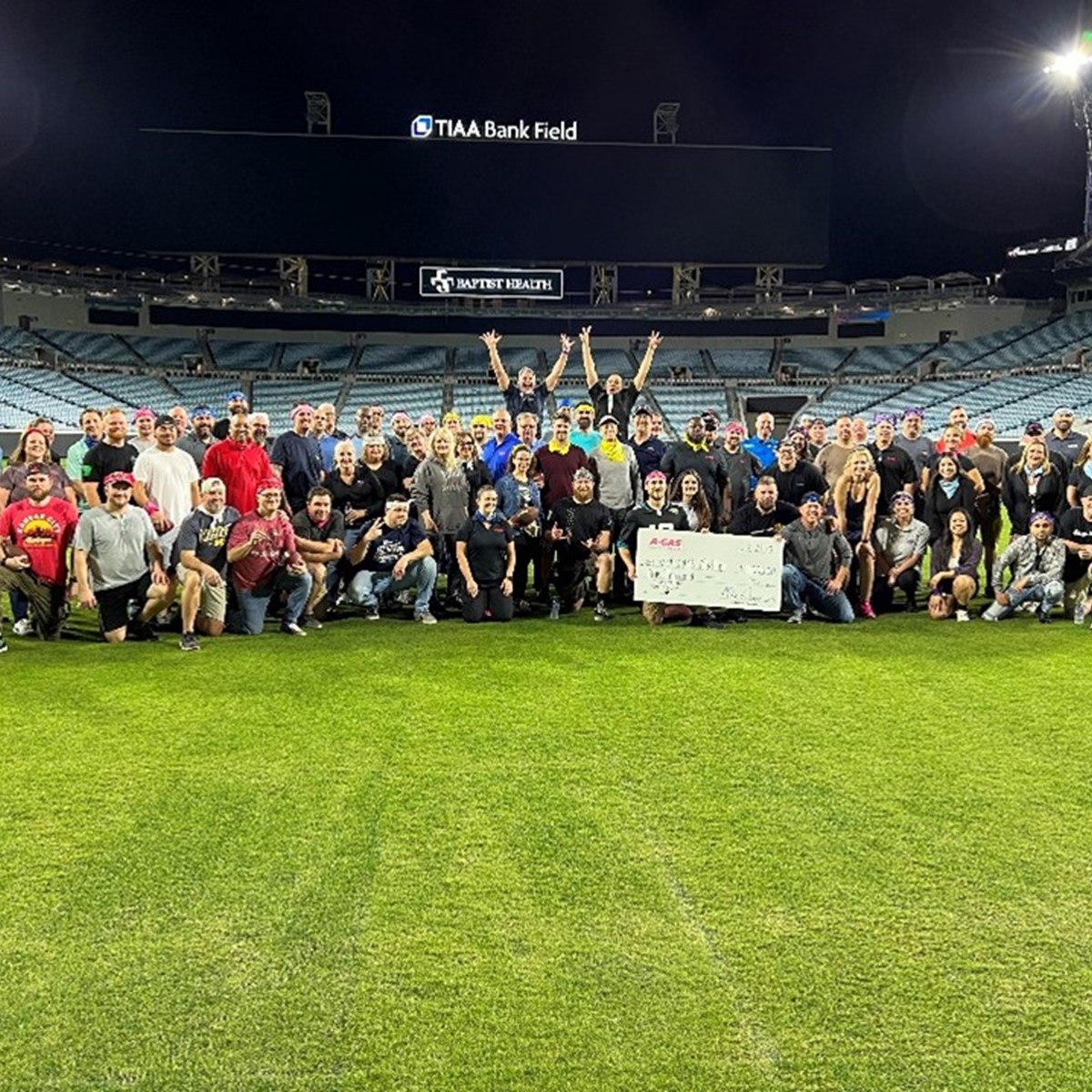 A large group of people stand on an American football while holding a large white check