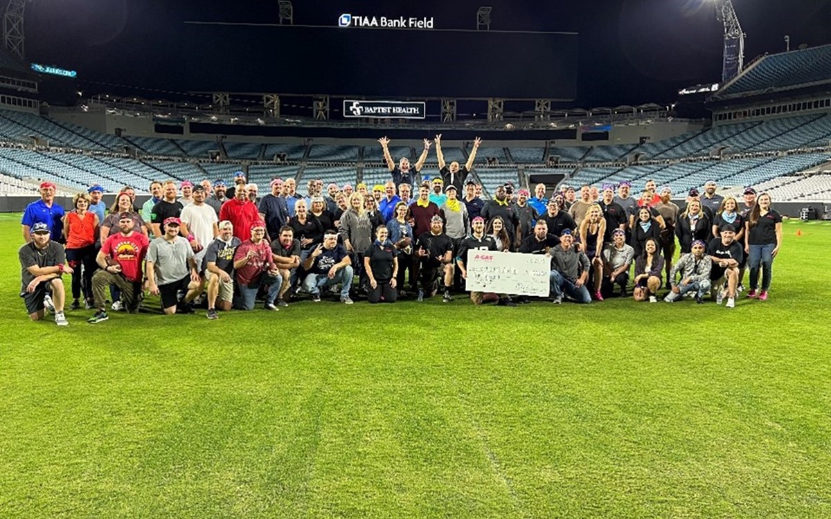 A large group of people stand on an American football while holding a large white check