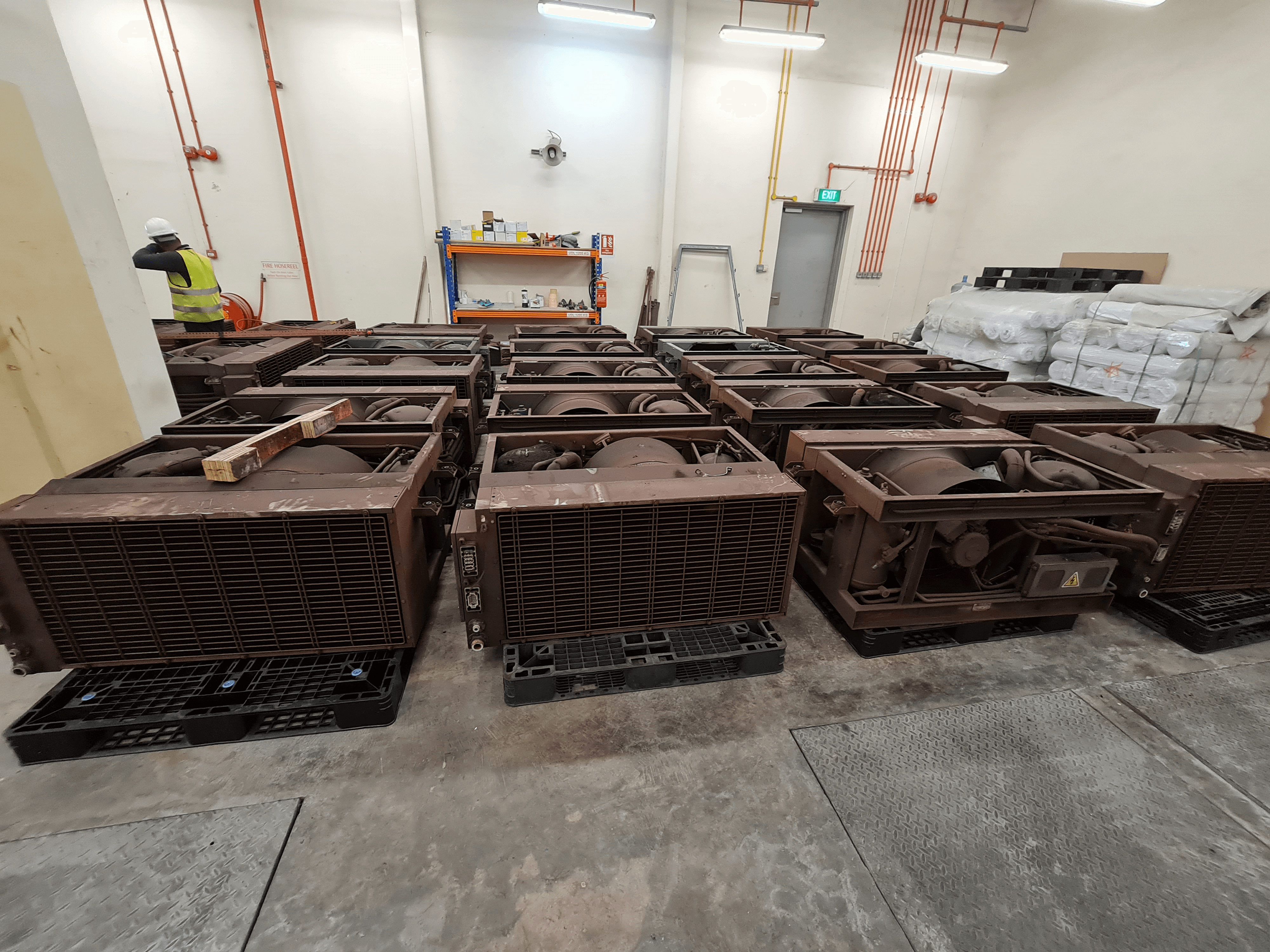 Large grey air conditioning units in a warehouse with a man in a yellow high-vis jacket in the background 
