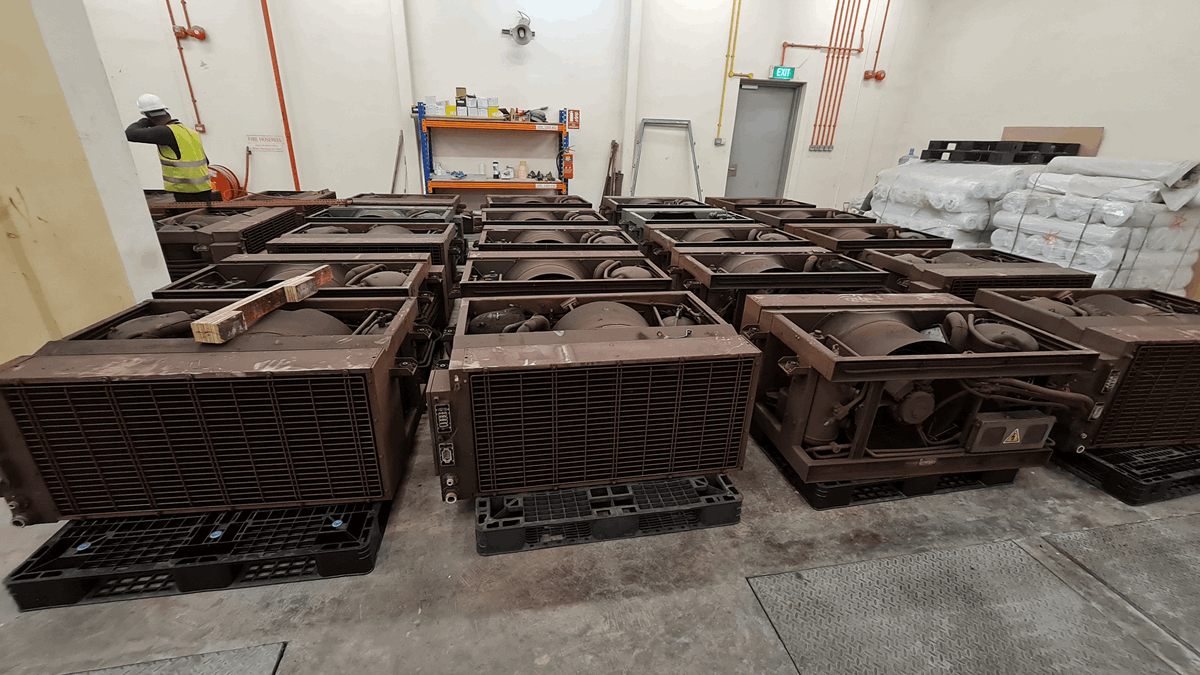 Large grey air conditioning units in a warehouse with a man in a yellow high-vis jacket in the background