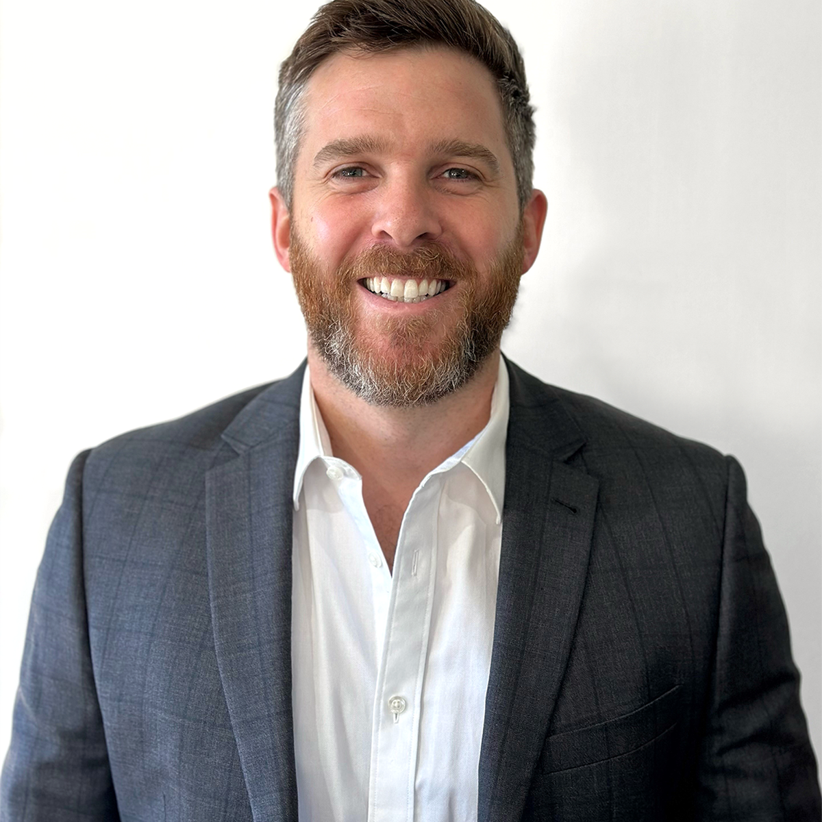 A man in a white shirt and grey jacket smiling at the camera