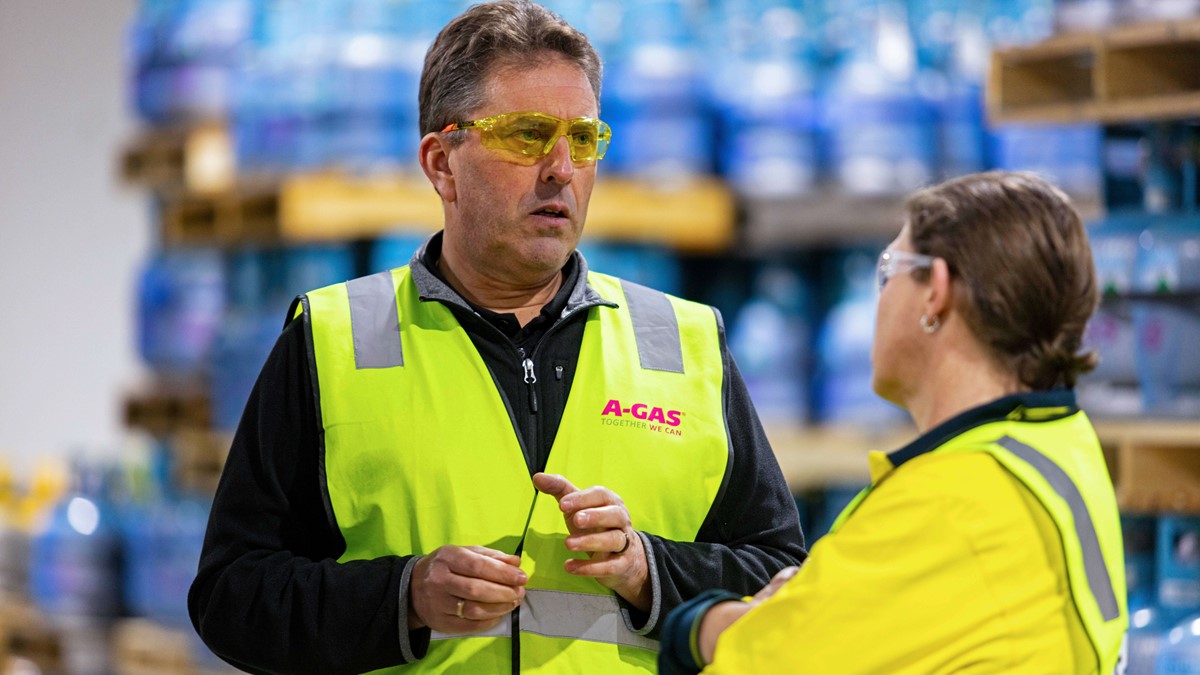 A man and a woman in high-vis jackets talking in a warehouse
