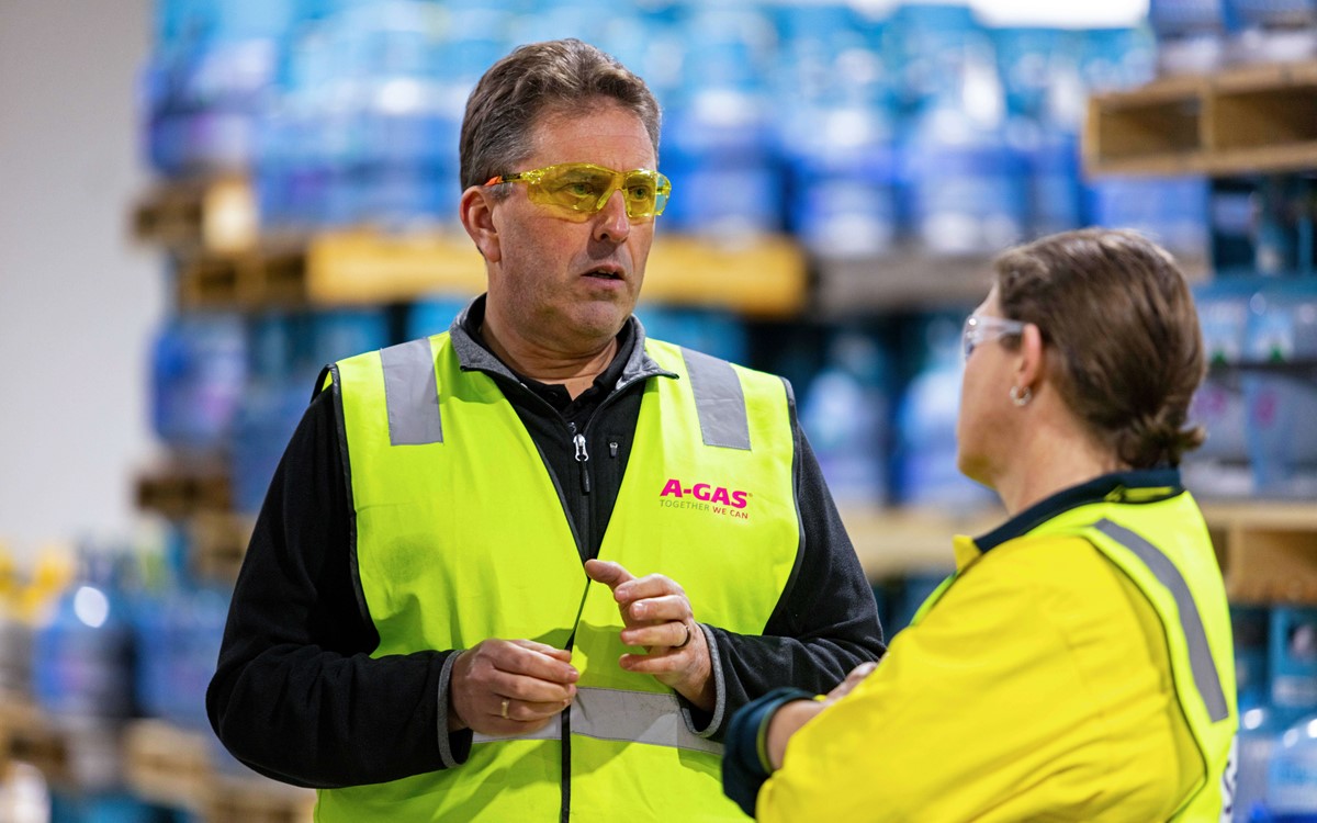 A man and a woman in high-vis jackets talking in a warehouse