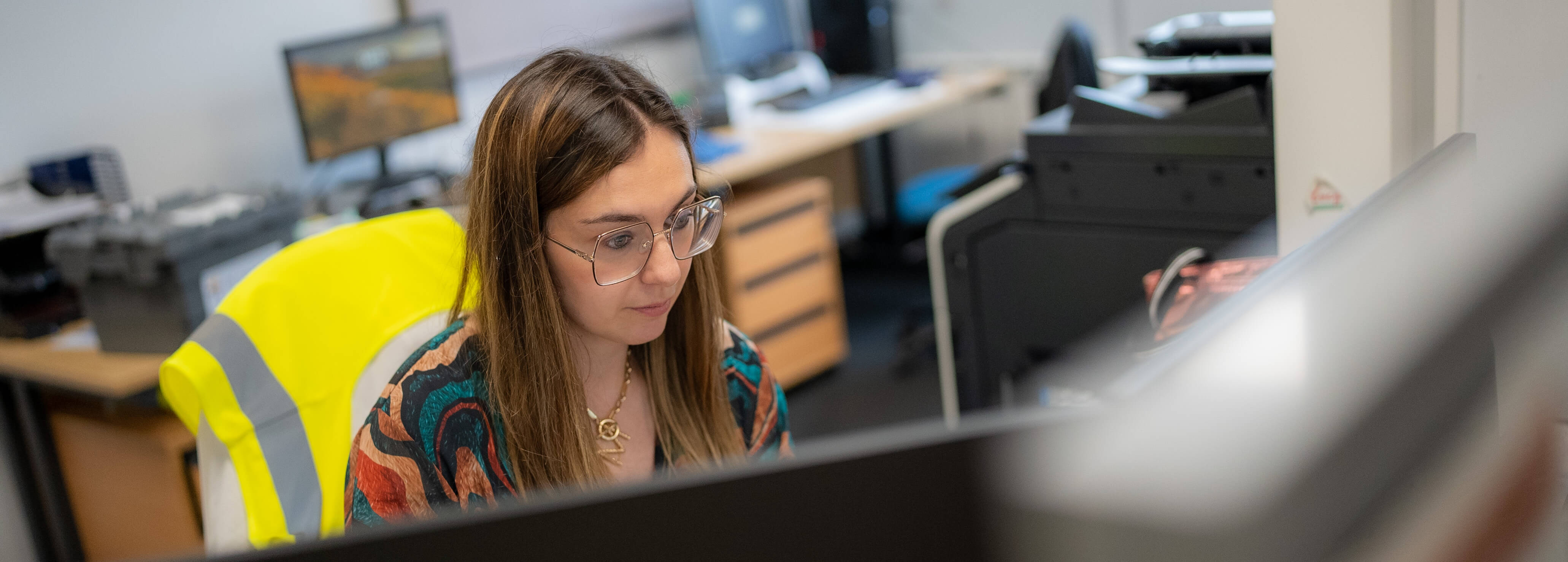 A woman wearing glasses and multi-coloured shirt working at a computer 