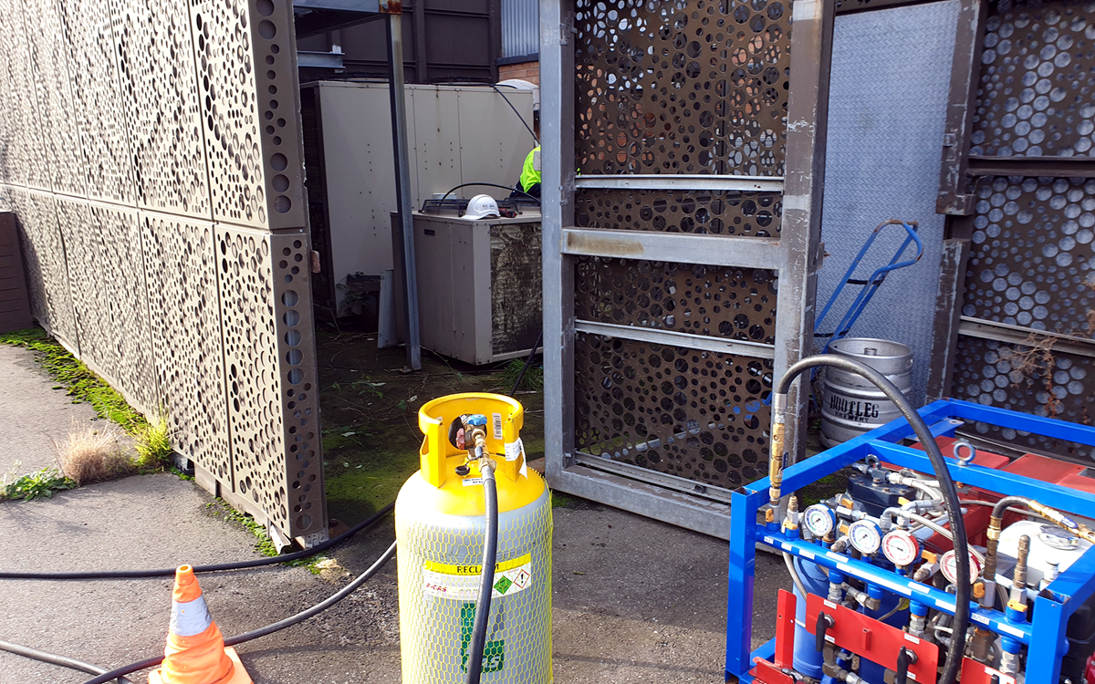 A close-up of a grey recovery cylinder attached to a blue recovery unit on-site