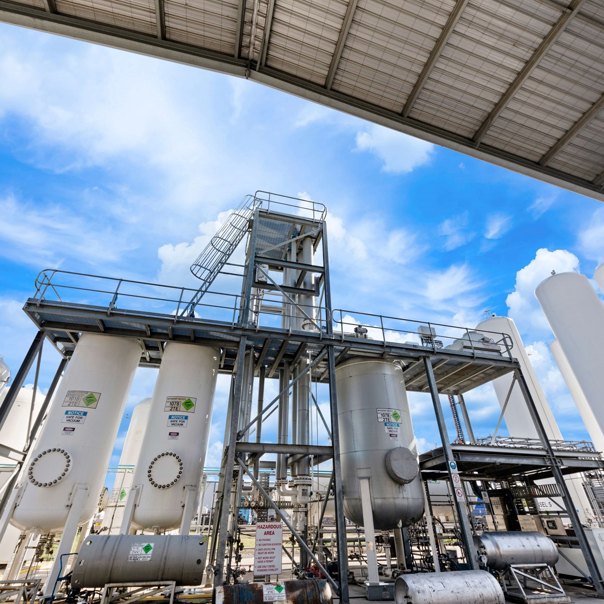 Multiple white separation towers surrounded by metal scaffolding, taken from underneath a metal roof