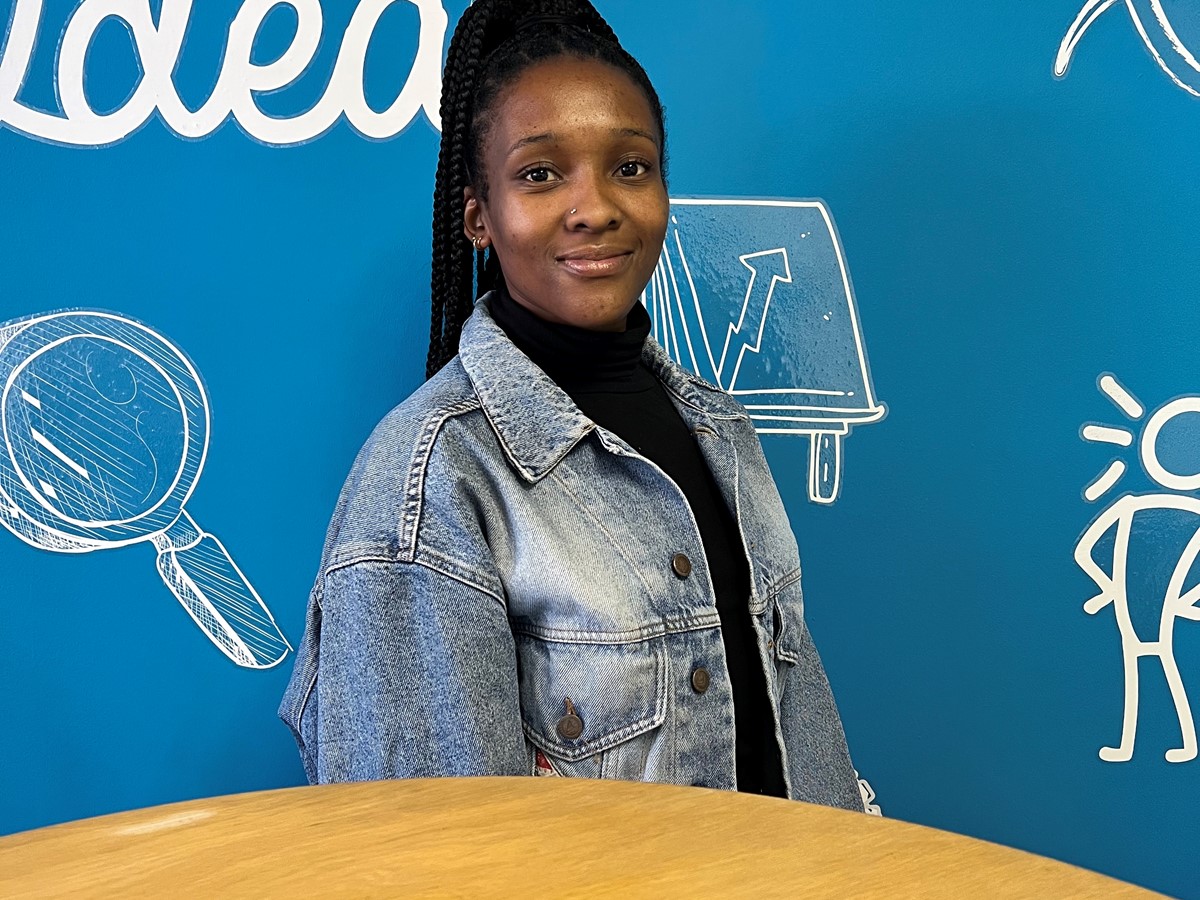 A woman in a denim jacket smiling at the camera in front of a blue and white wall