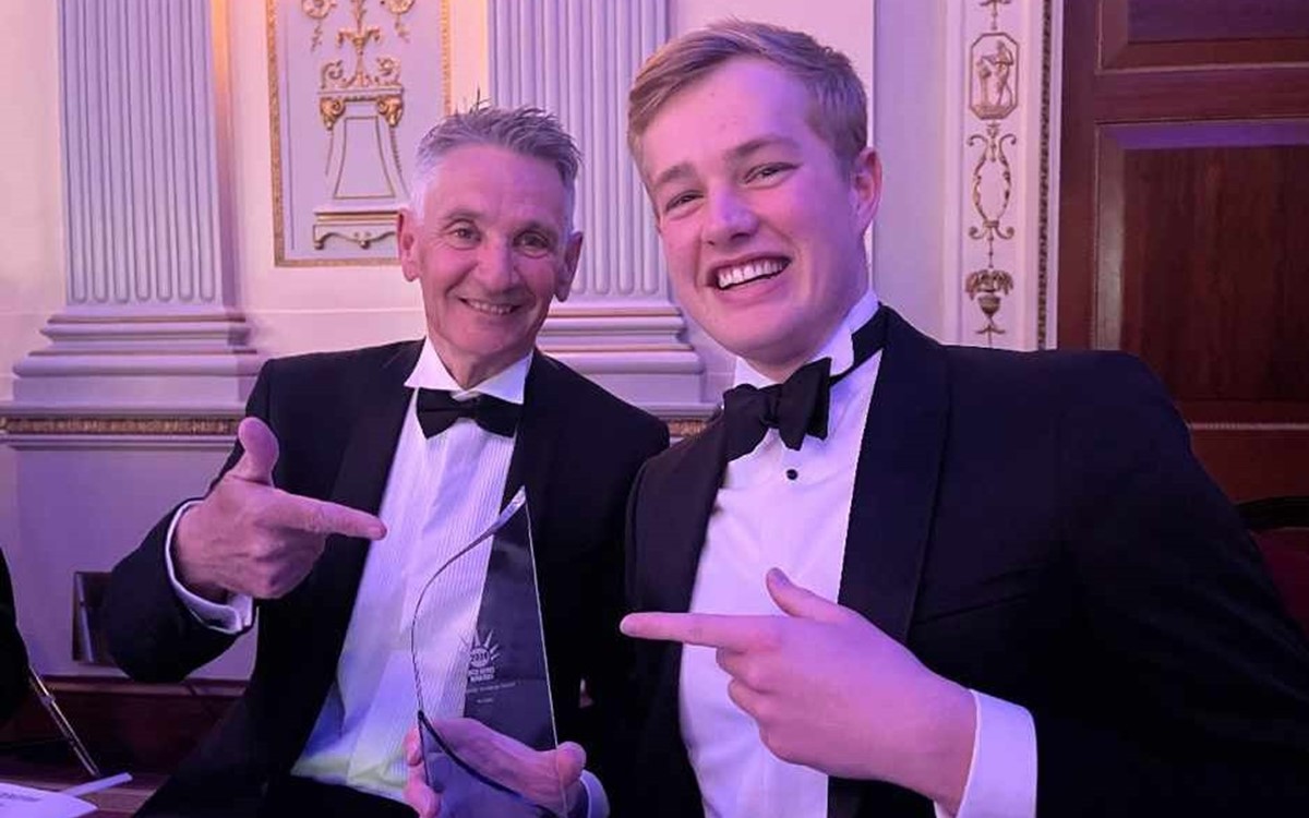 A close-up of two smartly dressed men smiling and pointing towards an award they are holding