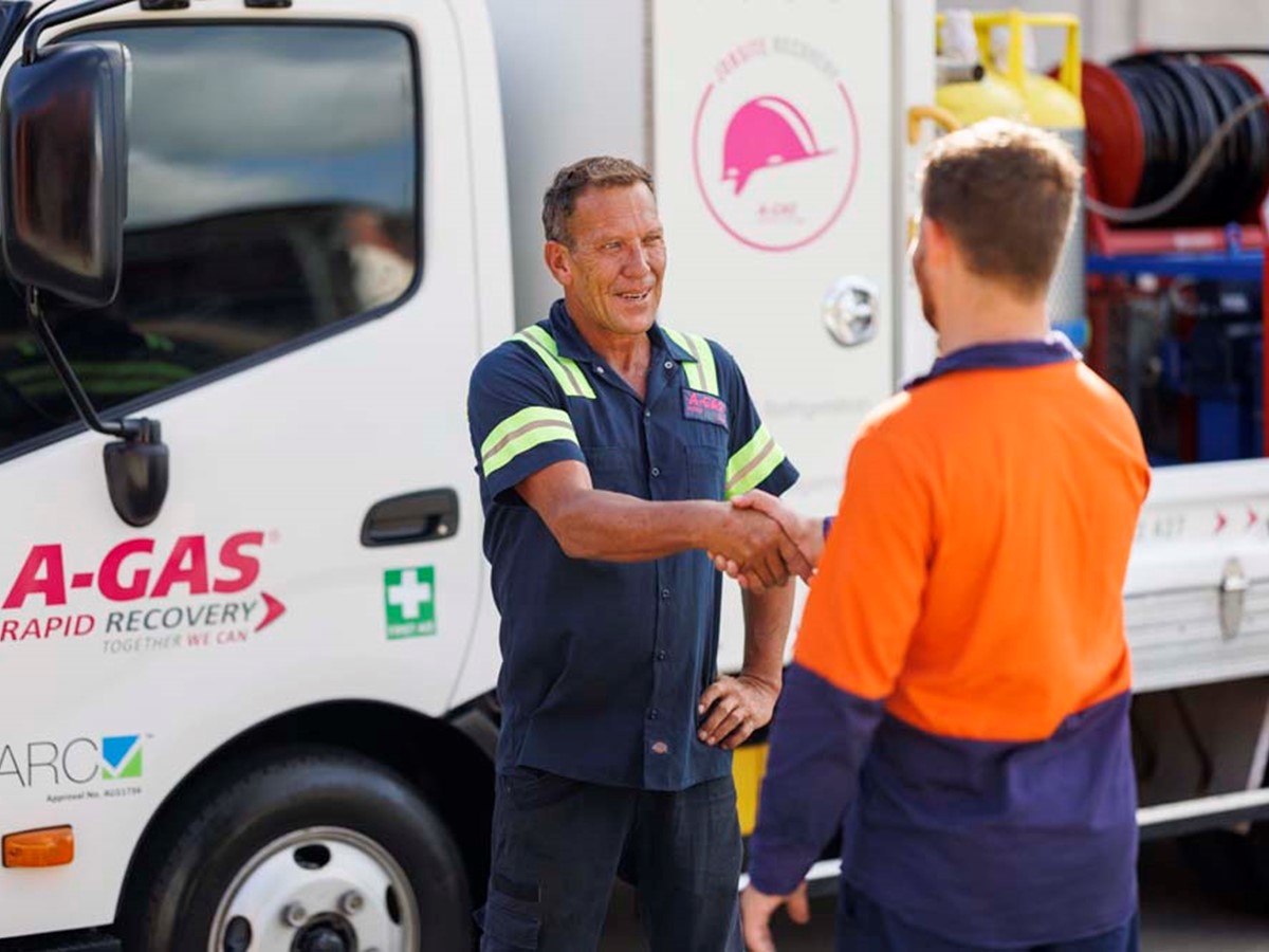 Two men shaking hands next to a white recovery truck