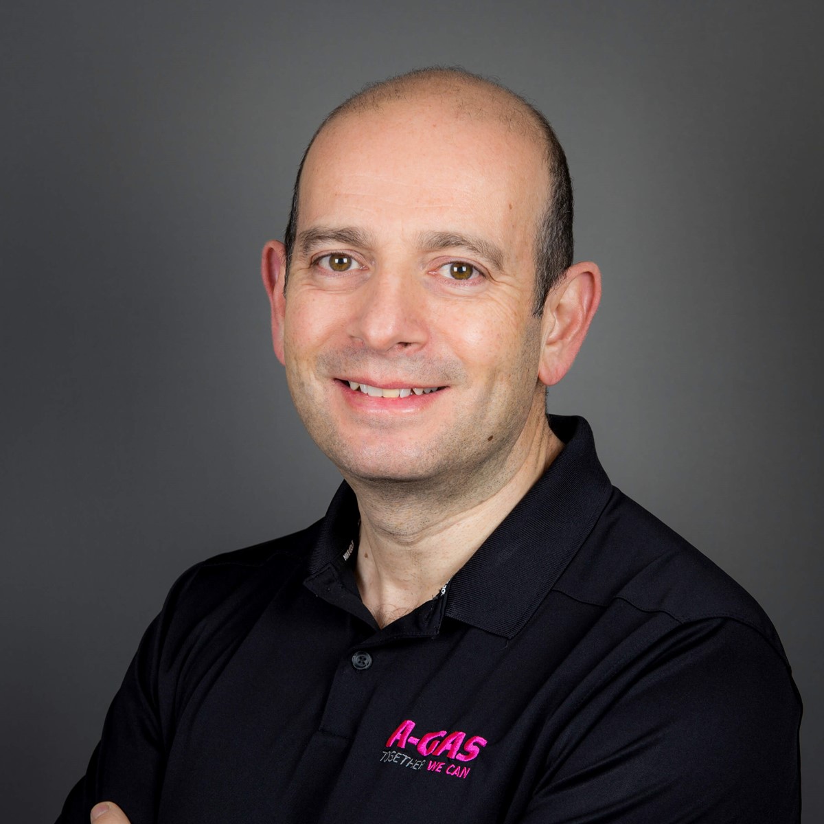 A headshot of a man in a black polo with a grey background