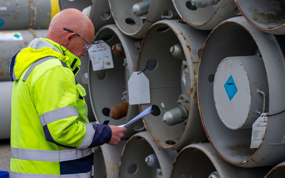 Man in a yellow hi-vis jacket reading in front of silver cylinders