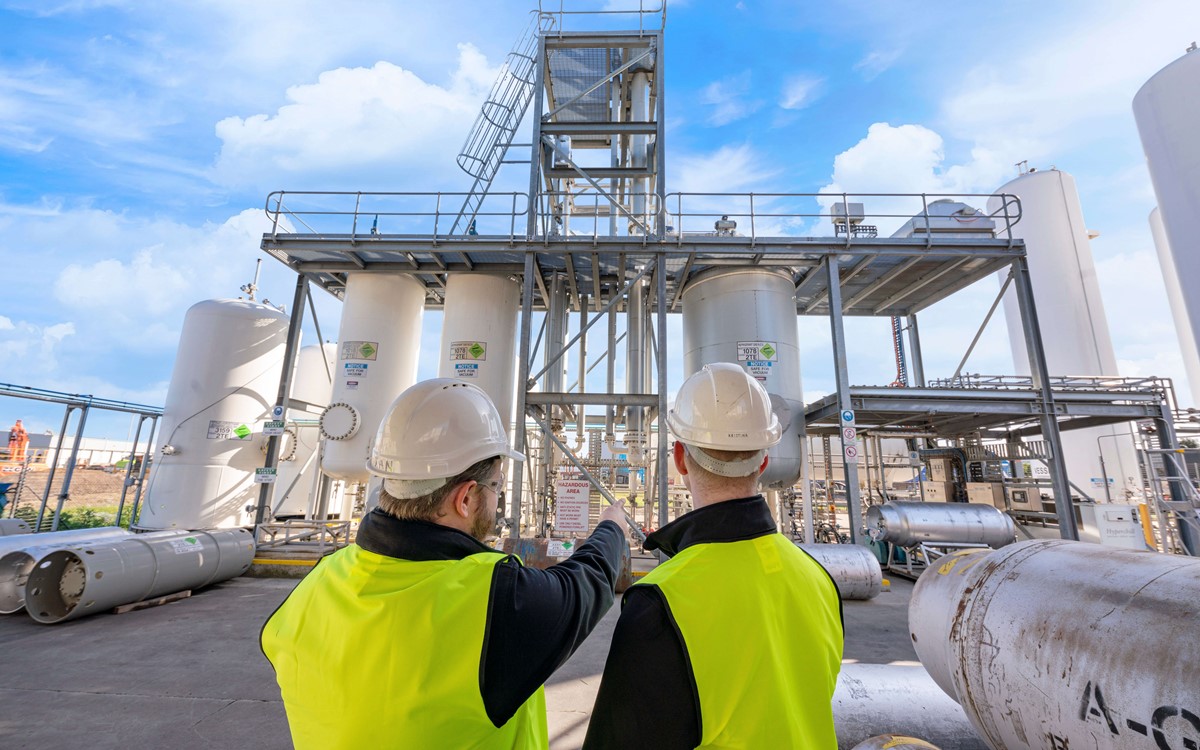 Two men in yellow high-vis jackets talking and pointing in front of white separation towers