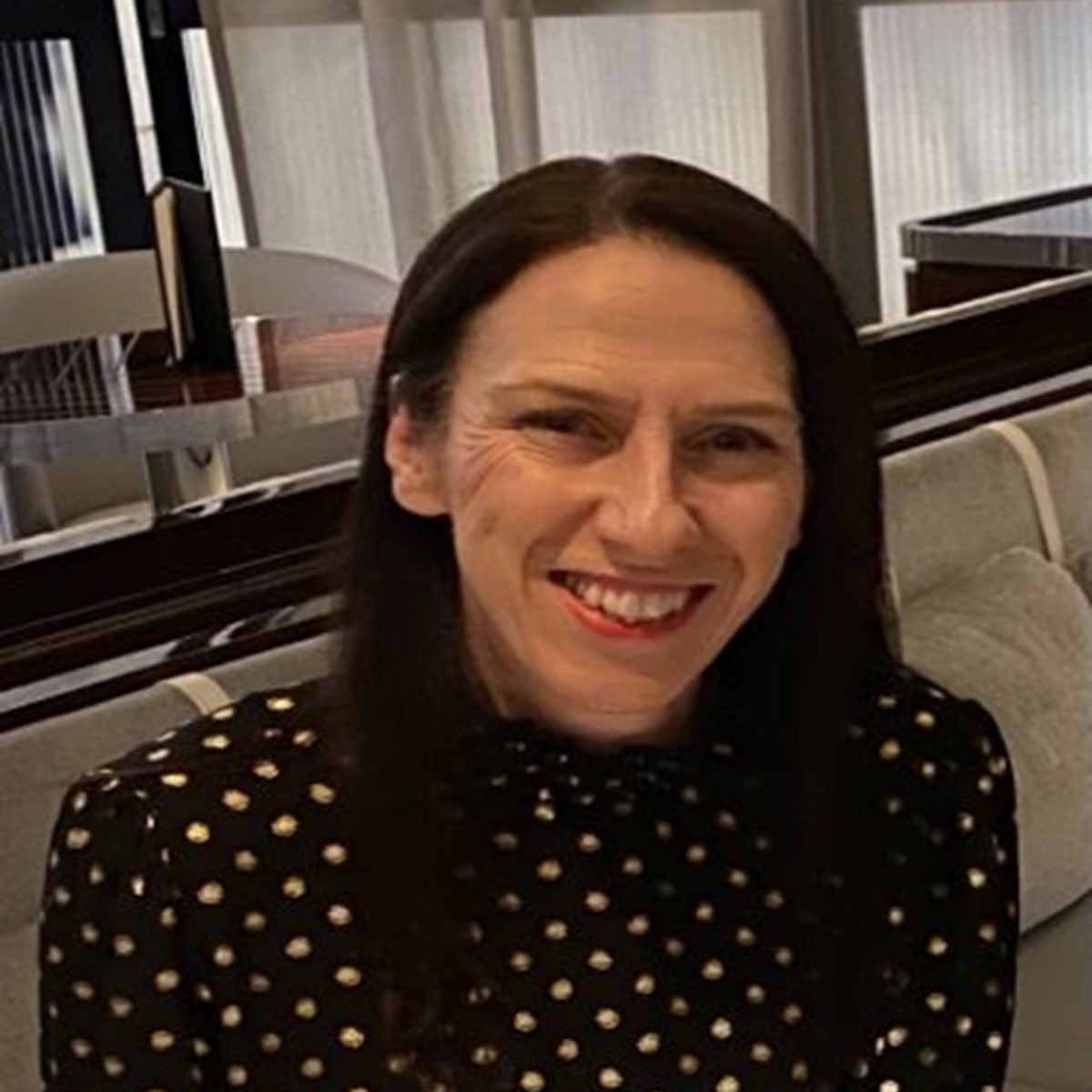 A woman in a black and white spotted shirt smiles at the camera in a restaurant setting
