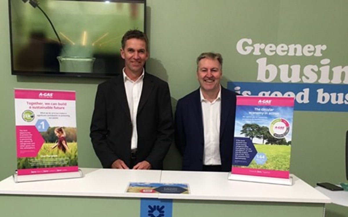 Two smartly dressed men standing behind a green counter and smiling at the camera