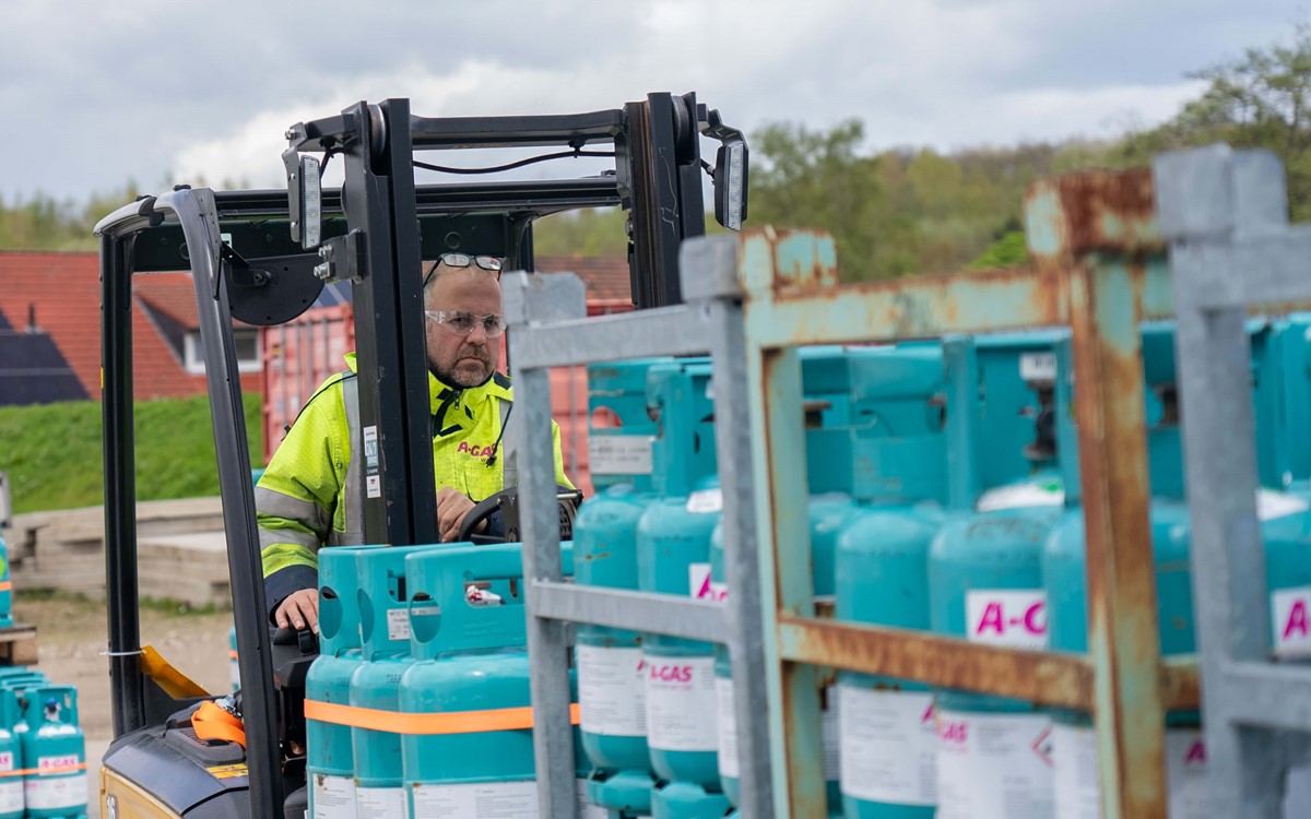 A man in a high-vis yellow jacket moving blue cylinders with a forklift truck