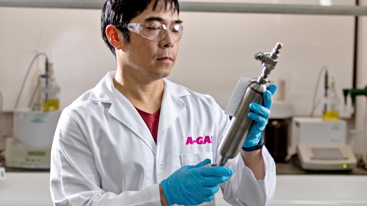 Technician in a white coat holding a silver metal tool in a laboratory