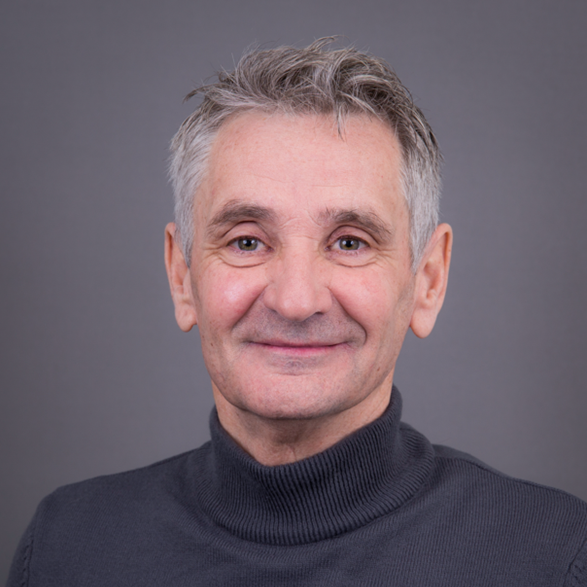 A headshot of a man smiling at the camera against a grey background