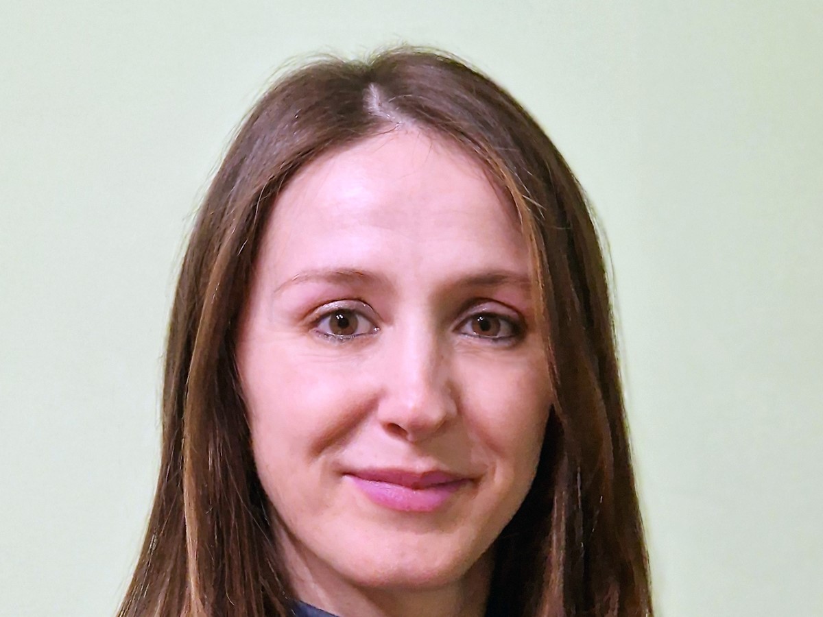A headshot of a woman in a denim jacket smiling against a light grey background