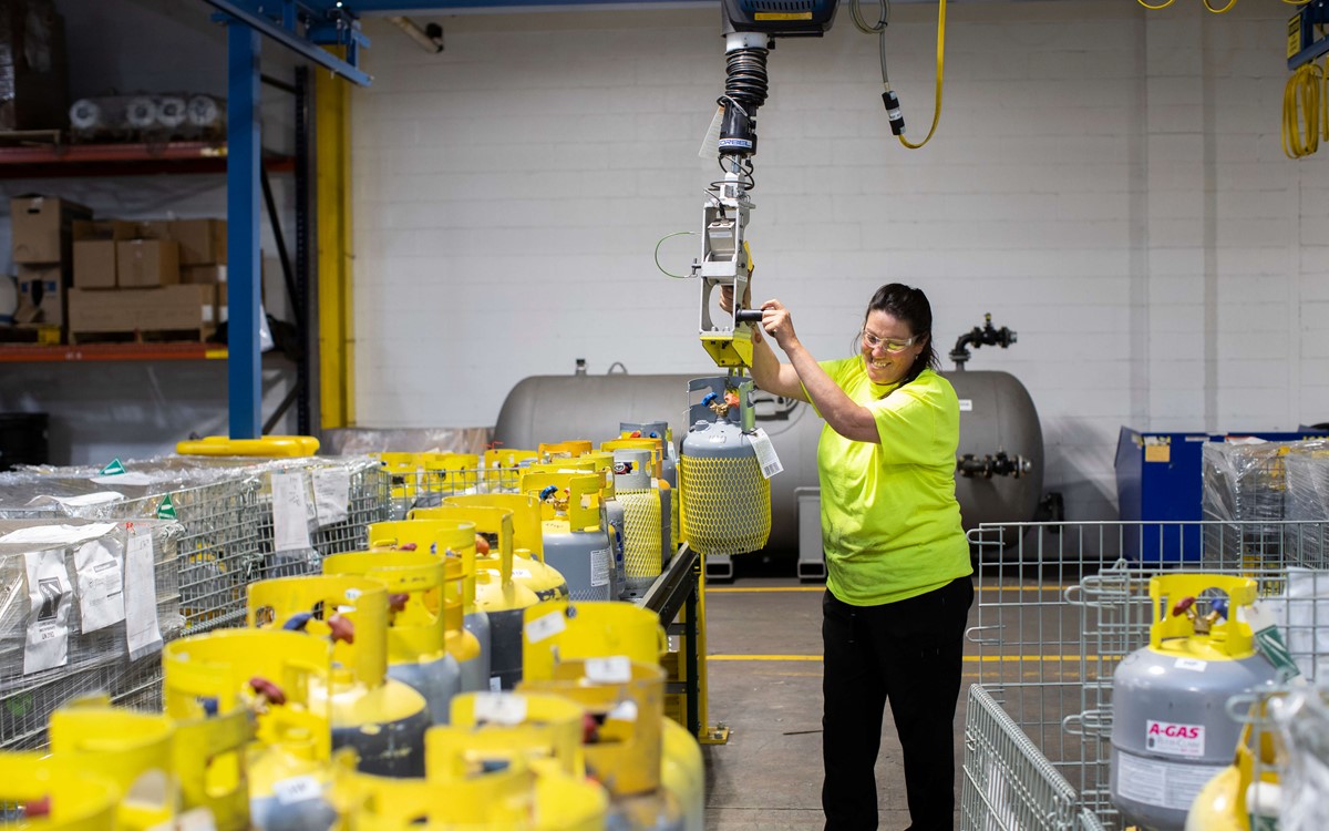 A woman in a warehouse operating a crane above metal baskets full of gas cylinders
