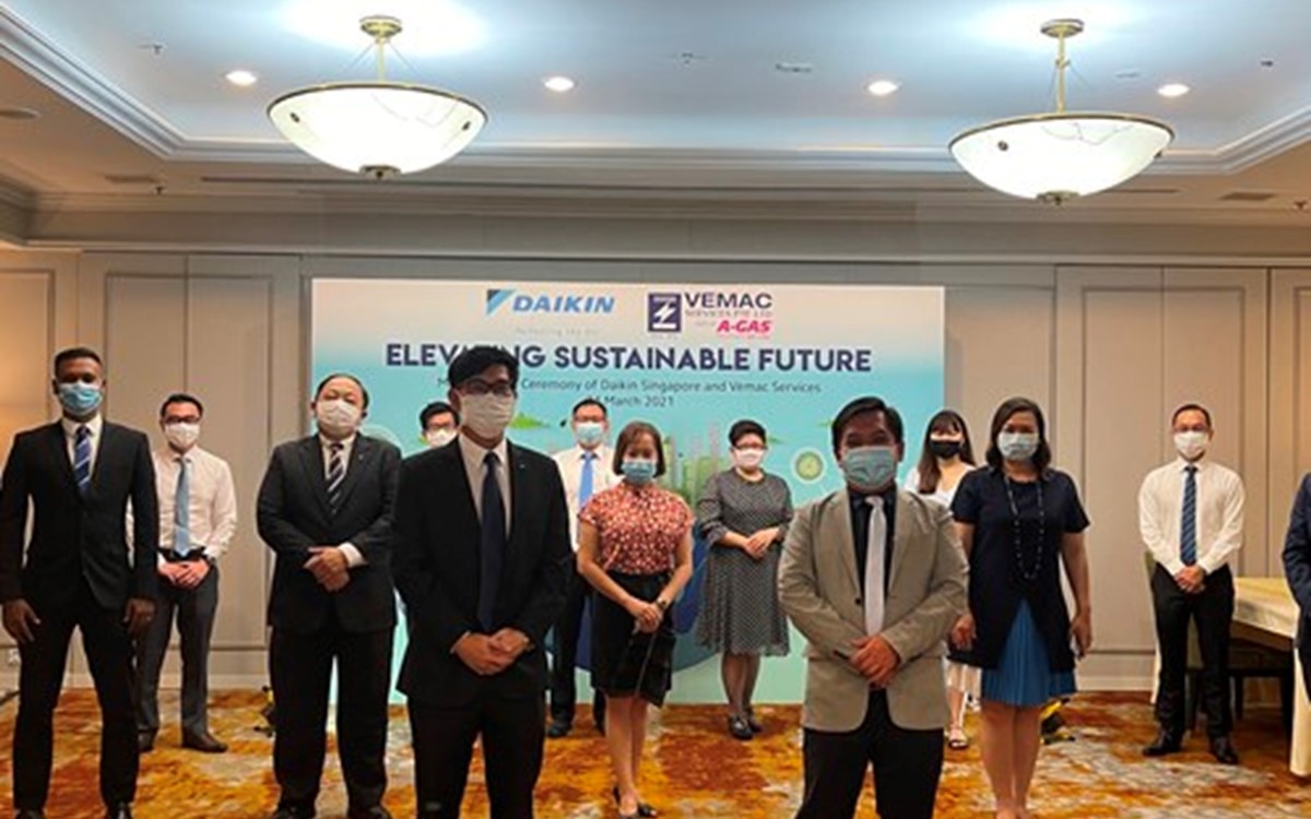 A group of people wearing facemasks stand in front of a poster looking at the camera