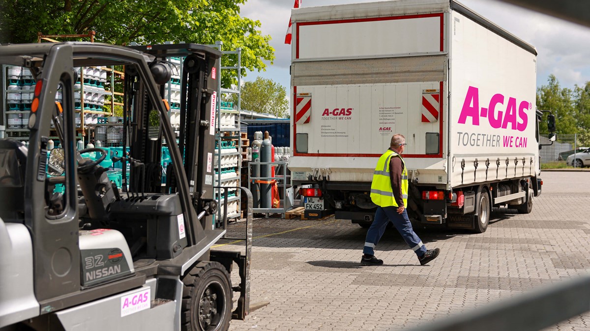 A man in a yellow high-vis jacket walks between a forklift and a white lorry with the pink A-Gas logo