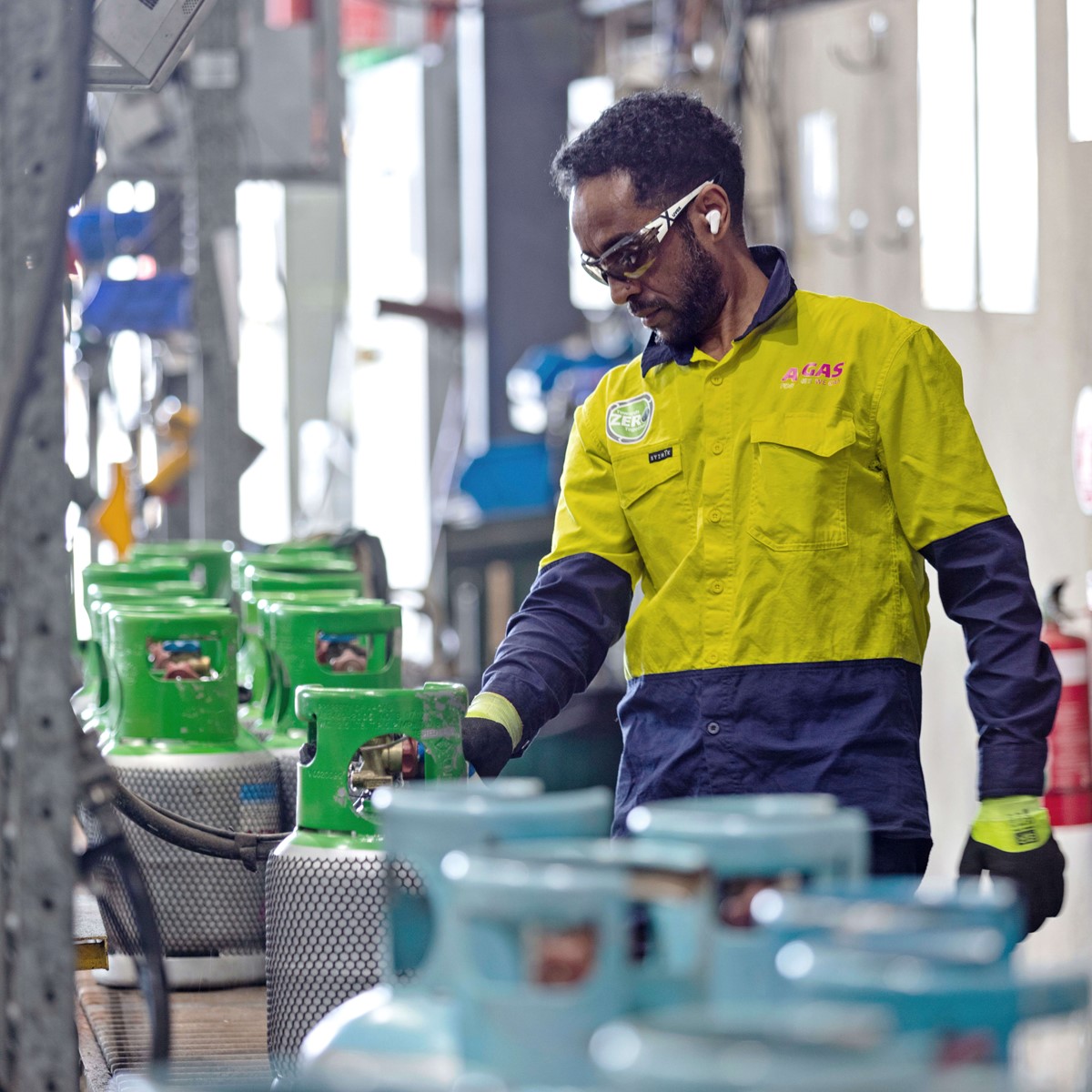 Technician in a yellow and blue high-vis jacket working with a green-topped gas cylinder in a warehouse