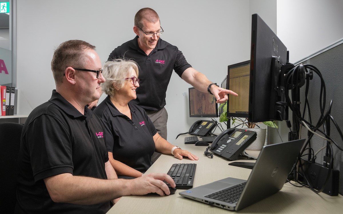 Man pointing at computer screen while smiling next to colleagues in an office