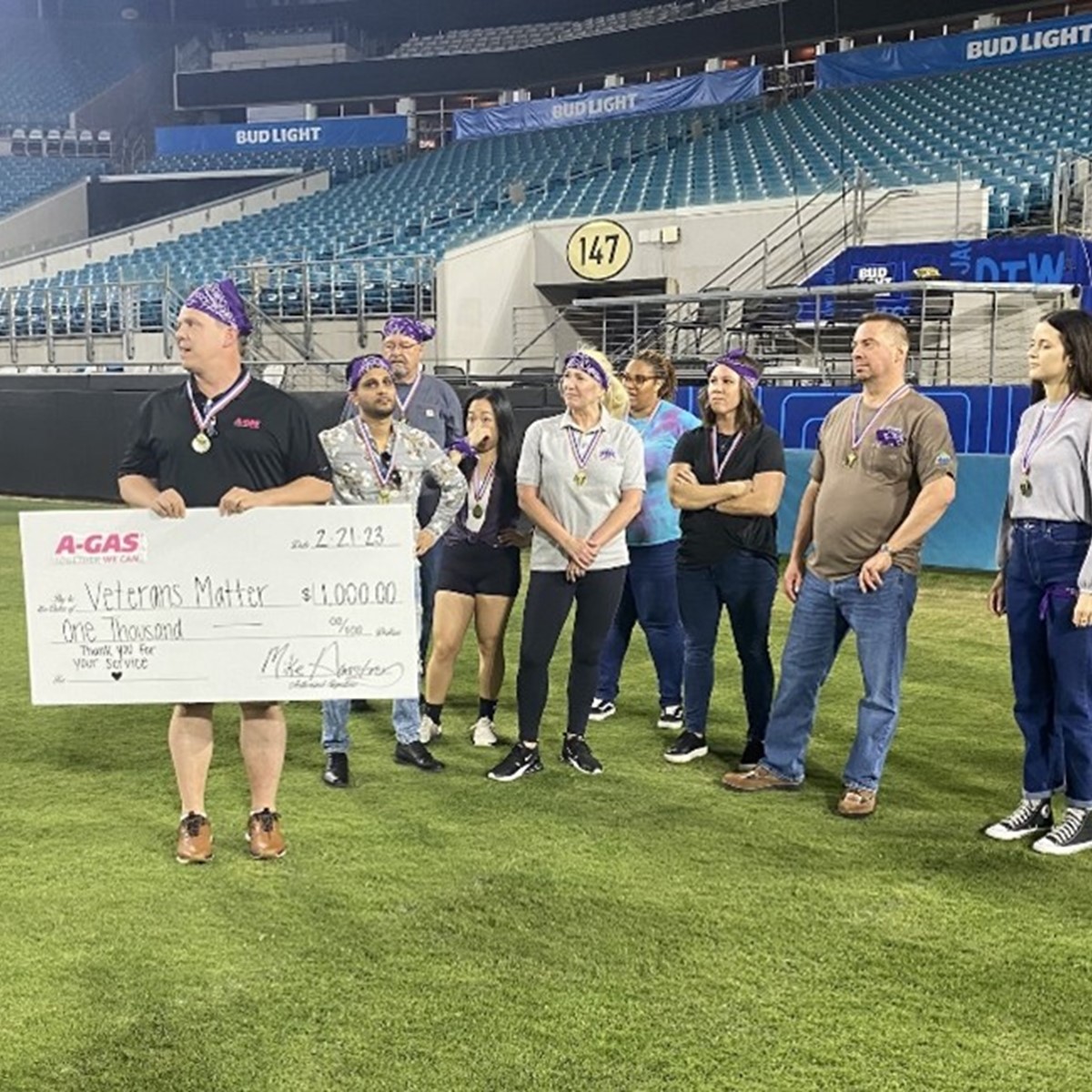 A group of people stand on an American Football field with a man holding a large white check