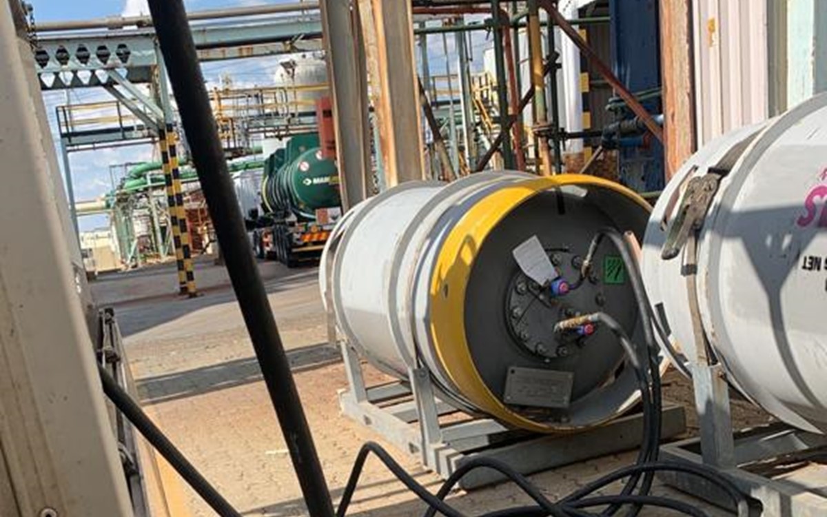A large grey drum attached to equipment by black hosing on-site