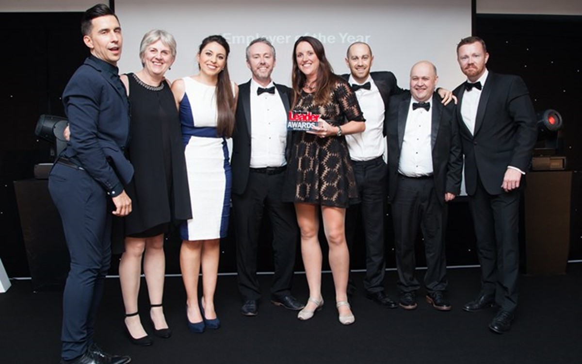 A group of smartly dressed people being presented with an award in front of a screen