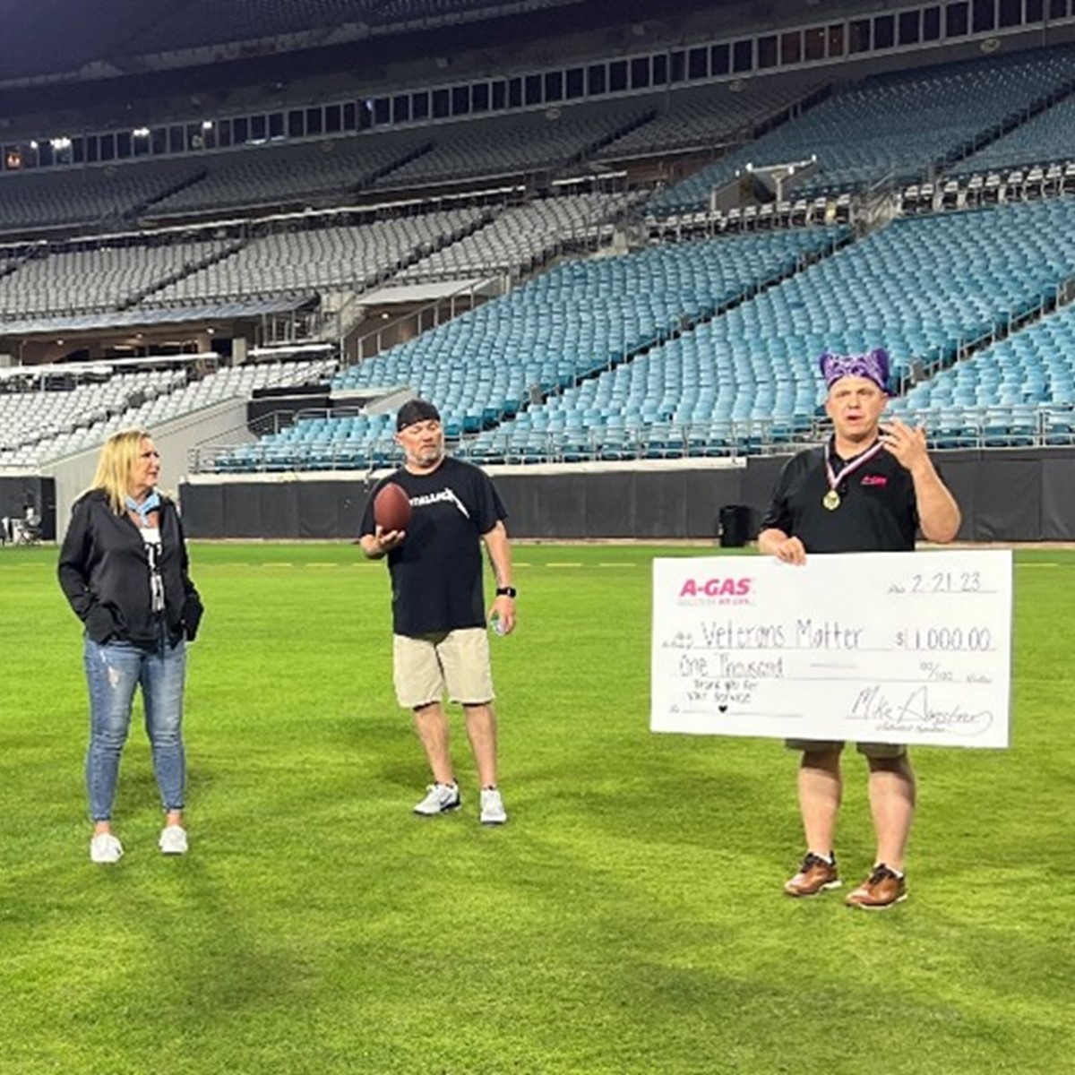 A group of people stand on an American Football pitch and a man holding a big white check