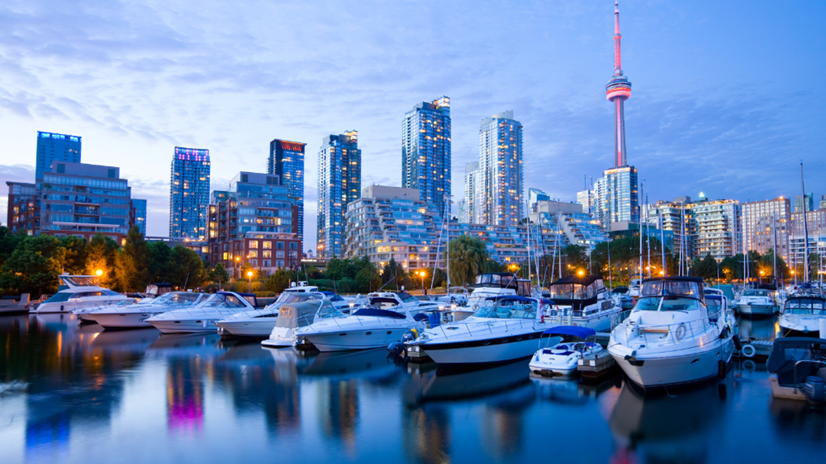 A city in Canada at night, there are boats parked on the water with the city lights of the buildings in the background reflecting in the water