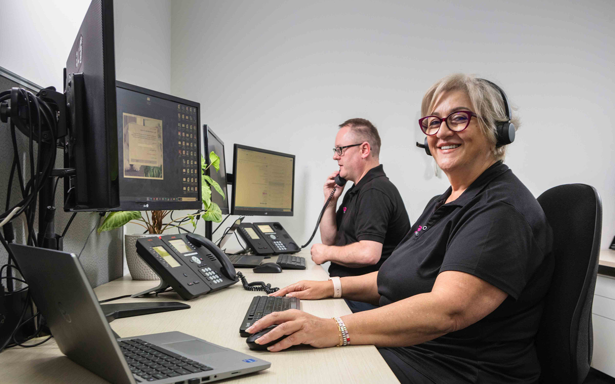 A woman in a headset working at a computer while smiling at the camera