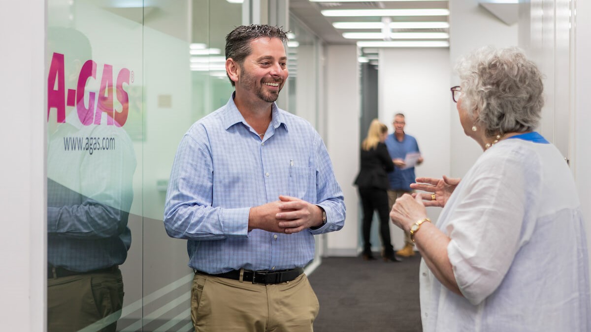 A man in a blue shirt smiling and talking to a woman in an office corridor