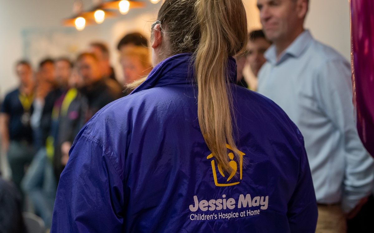 A woman in a purple jacket with her back to the camera talks to a group of people