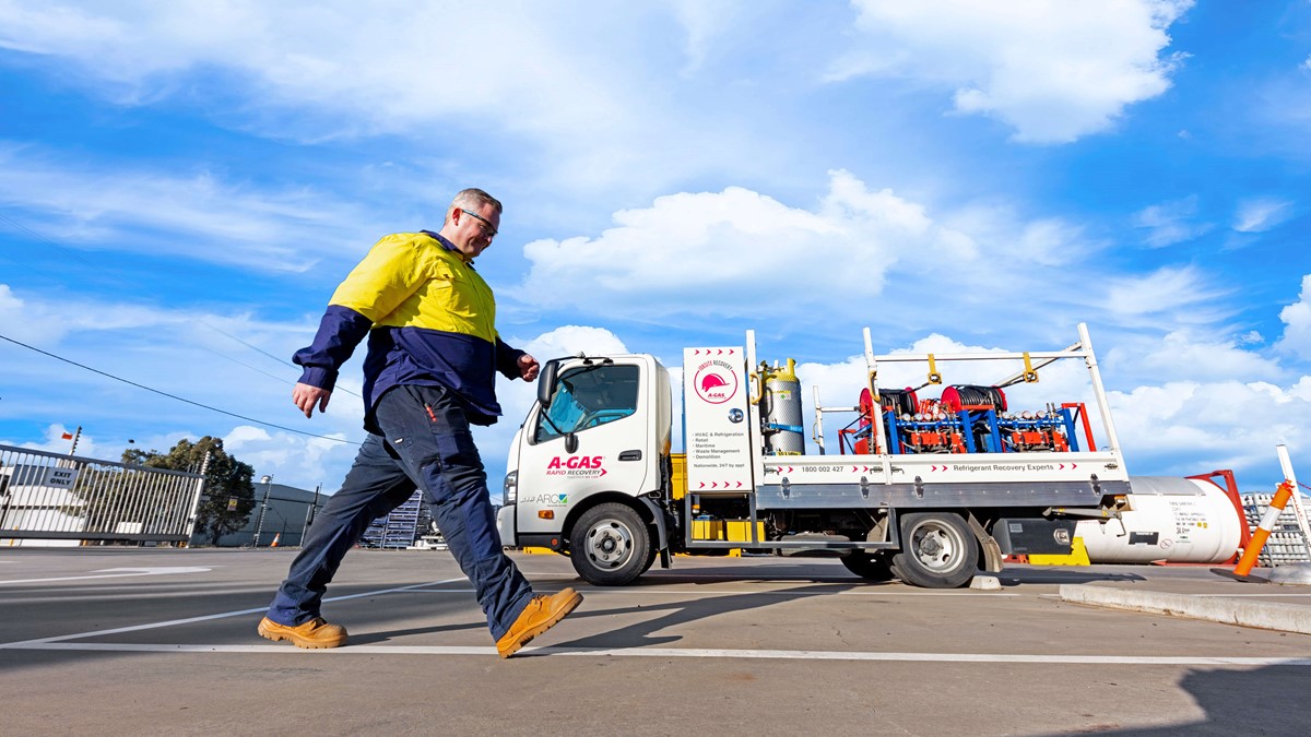 Man walking across a carpark in front of a white A-Gas recovery truck with equipment on the back
