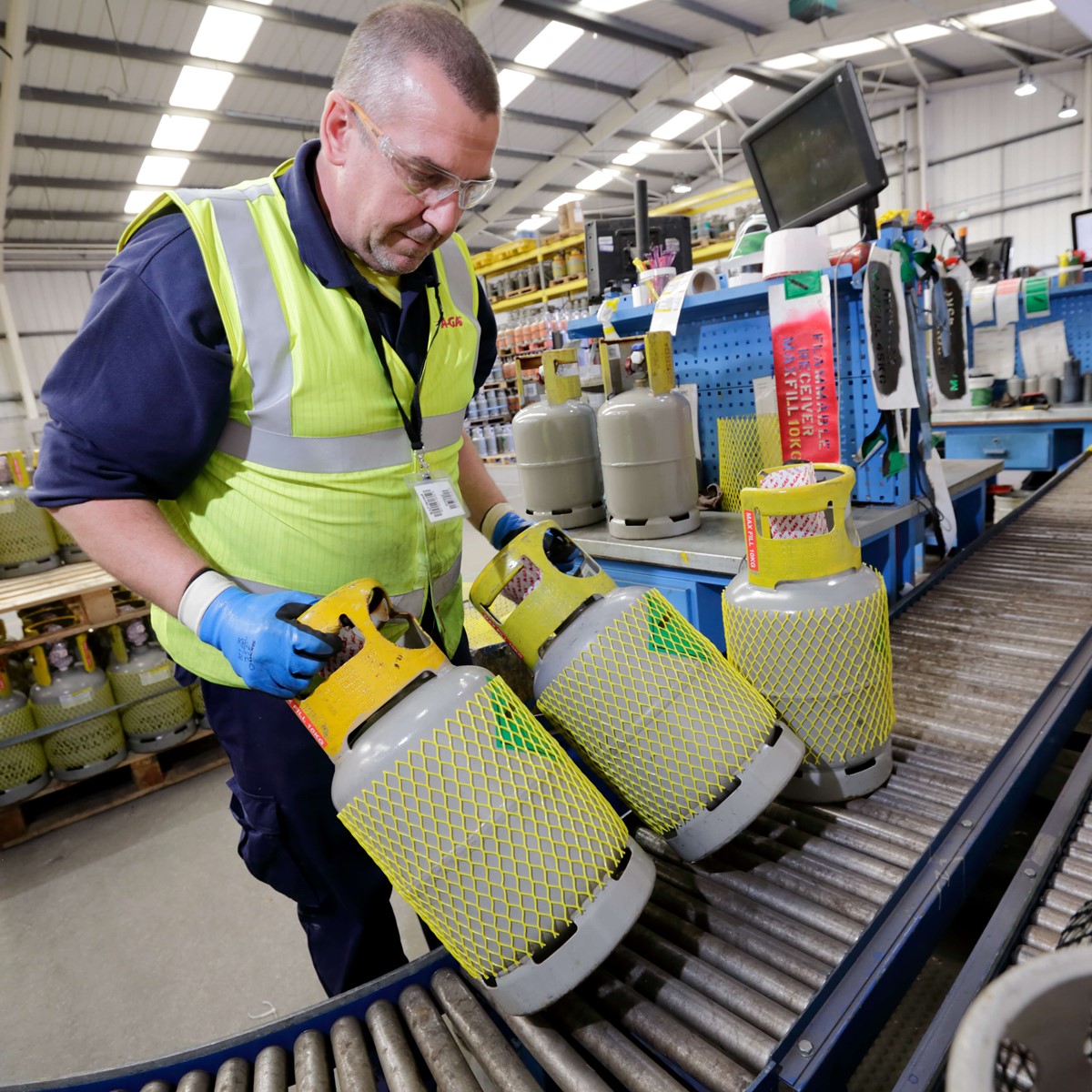 A man working in a warehouse, he is wearing a hi vis jacket and moving gas cylinders