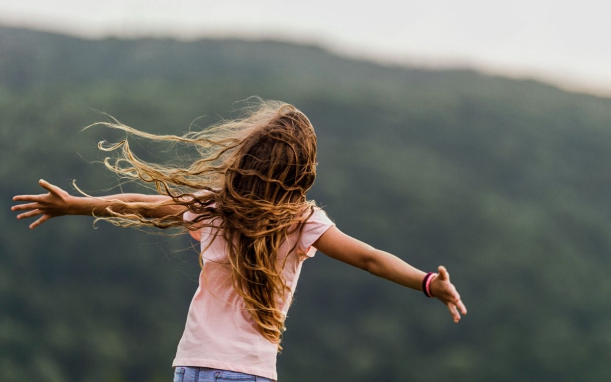 young girl with back to camera with arms wide open embracing nature