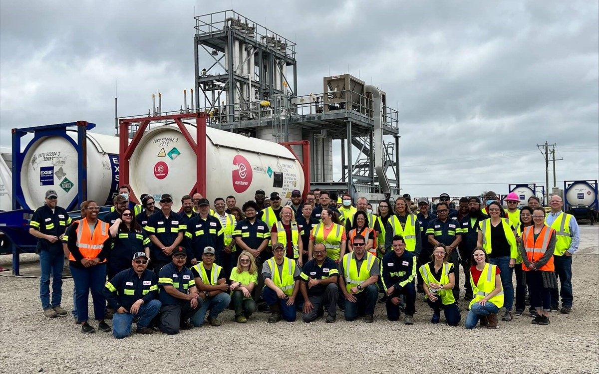 A team of warehouse workers outside lined up underneath industrial gas cylinders