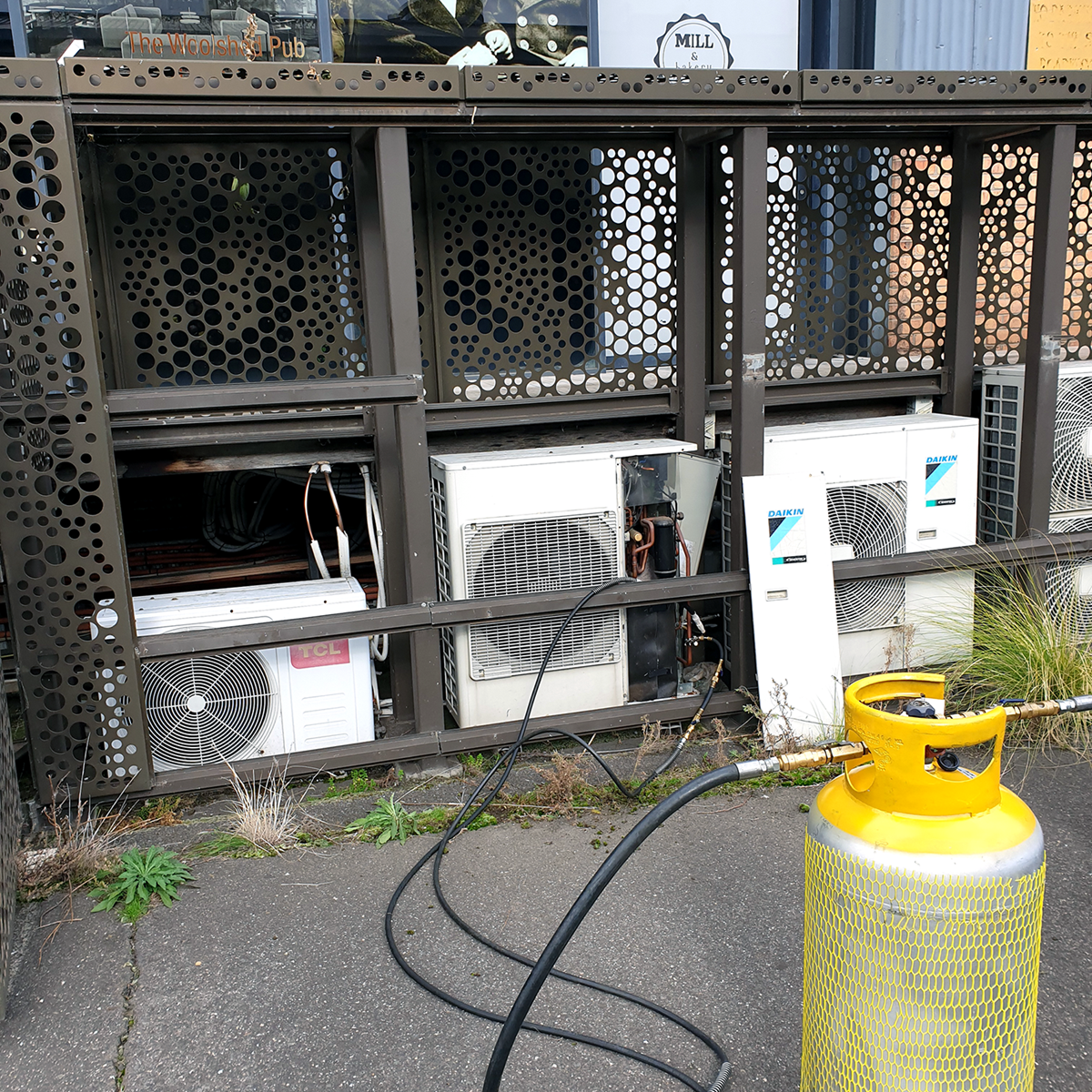 A grey recovery cylinder attached to three white air conditioning units on-site