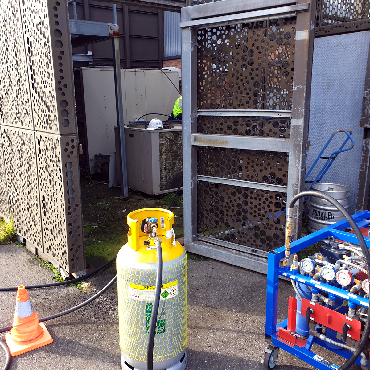 A close-up of a grey recovery cylinder attached to a blue recovery unit on-site